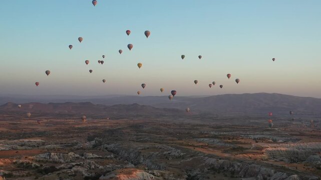 Aerial view of hot air balloons dotting the dusky sky over the expansive landscape creating a stunning contrast of colors, Cappadocia, Turkey.
