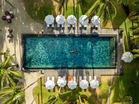 Aerial view of a turquoise pool reflecting the sky, fringed by white umbrellas and verdant palms, a serene oasis, Prince Maurice, Flacq District, Mauritius.