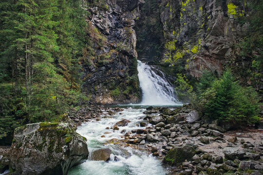 A powerful waterfall cascading over steep cliffs into a rocky stream bed, surrounded by lush evergreen forests in the Reinbach Gorge near Sand in Taufers.