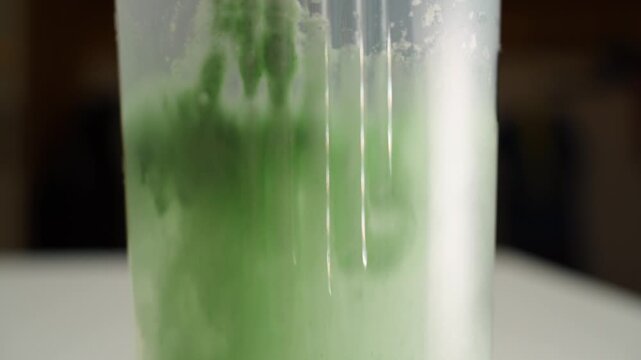 Green creatine powder being thrown into a shaker with water, close-up