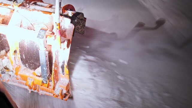 Close and elevated views of a snowplow blade pushing heavy snow off a highway at night. Blowing snow, icy asphalt and warning lights capture intense winter conditions and active road maintenance work.