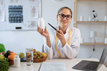 Portrait of woman nutritionist doctor demonstrating pills bottle at camera in office. food expert...