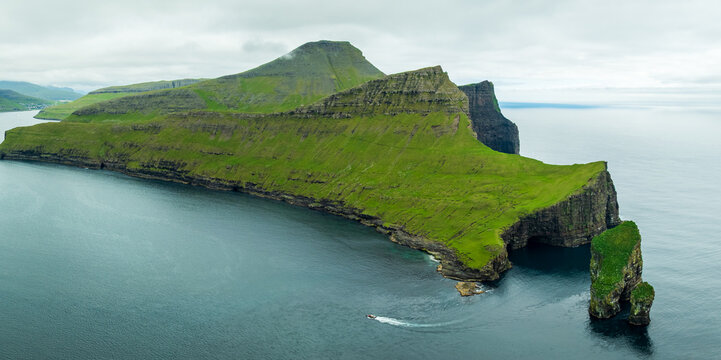 Aerial view of the dramatic, towering cliffs of Tindholmur island meet the vast, cool ocean under a cloudy sky, Tindholmur, Faroe Islands.