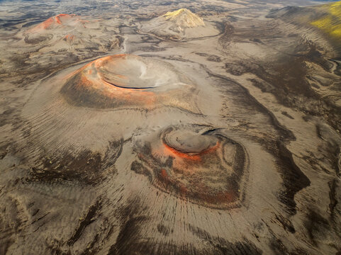 Aerial view of a surreal, Martian landscape where red volcanoes pierce the ochre earth, their fiery crests contrasting starkly with the muted tones, red volcanoes, Iceland.