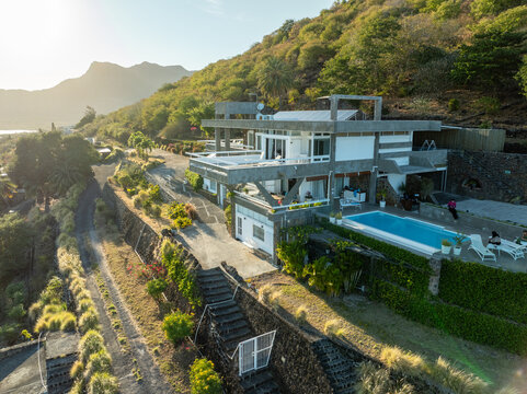 Aerial view of a modern villa nestled on a verdant hillside overlooking the azure sea, a serene contrast of architectural lines against nature's curves, Le Morne, Riviere Noire District, Mauritius.