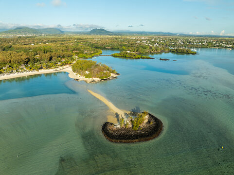 Aerial view of a small islet ringed by dark rocks and surrounded by turquoise waters near the shore, Shangri La, Trou d'Eau Douce, Mauritius.