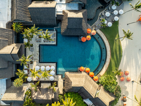 Aerial view of the resort's turquoise pool, nestled between thatched roofs and bright parasols, contrasting with the surrounding lush greenery, Prince Maurice, Flacq District, Mauritius.