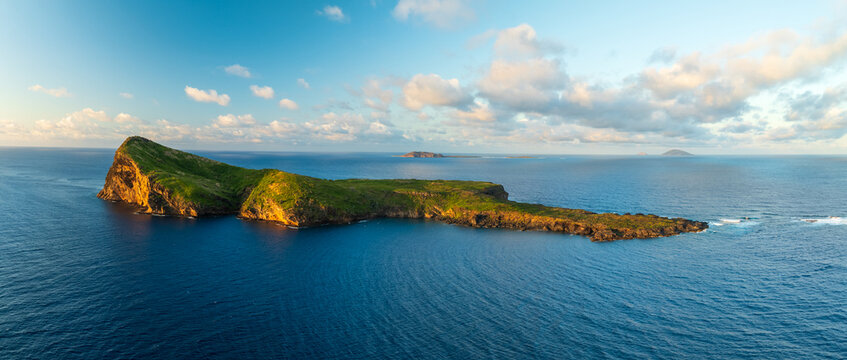 Aerial view of the rugged, sun-kissed cliffs meeting the deep blue sea, a tropical island paradise under a sky brushed with soft clouds, Coin De Mire, Mauritius.