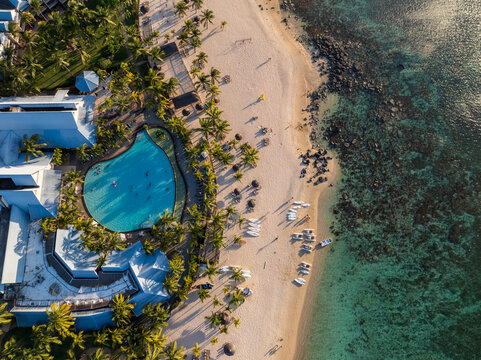 Aerial view of a pristine beach meeting turquoise waters, with palm trees lining the shore and a refreshing pool at a resort, Grand Baie, Riviere du Rempart District, Mauritius.