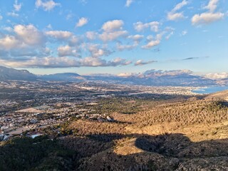 Fototapeta premium Sunshine illuminates hillside cityscape, Warm daylight highlights rolling terrain and distant coastlines