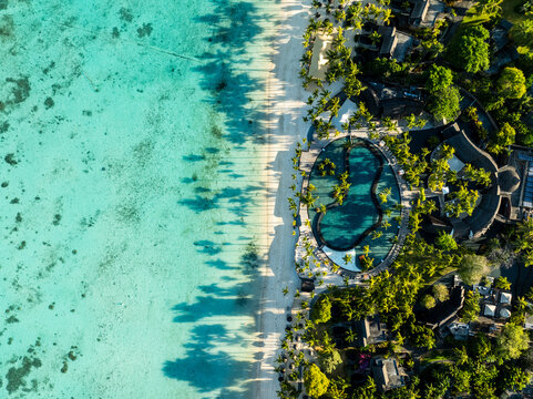 Aerial view of turquoise waters meet the pristine white sands, fringed by verdant trees and resorts along Royal Trou Aux Biches Rd, Triolet, Pamplemousses, Mauritius.