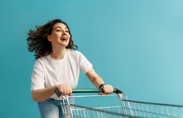 Happy Young Woman Enjoying Shopping with Cart on Blue Background ? Retail Lifestyle Concept © Konstantin Yuganov