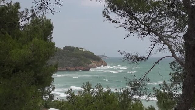 Playa de la Mora pine trees cliff tides waves wind overcast weather breakwater