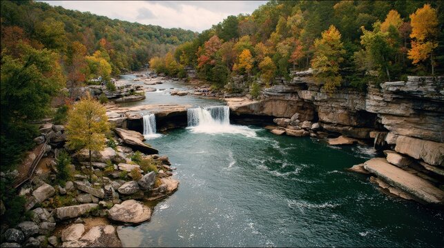 Wide view captures cascading water flowing between stratified rock formations amidst dense woodland during autumn