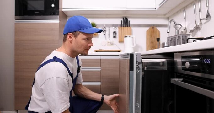 service worker installing integrated dishwasher in the kitchen. domestic appliance maintenance and repair