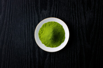 黒背景の木目に映える鮮やかな日本の抹茶パウダー　Vibrant Japanese matcha green tea powder on dark wood background