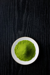 黒背景の木目に映える鮮やかな日本の抹茶の粉末　Vibrant Japanese matcha green tea powder on dark wood background