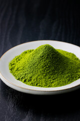 黒背景の木目に映える鮮やかな日本の抹茶パウダー　Vibrant Japanese matcha green tea powder on dark wood background