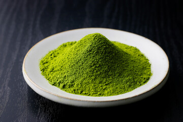 黒背景の木目に映える鮮やかな日本の抹茶パウダー　Vibrant Japanese matcha green tea powder on dark wood background