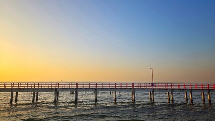 Fototapeta premium Scenic view of a red bridge with red railings at the ocean during sunrise.