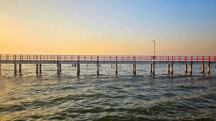 Obraz premium Scenic view of a red bridge with red railings at the ocean during sunrise.