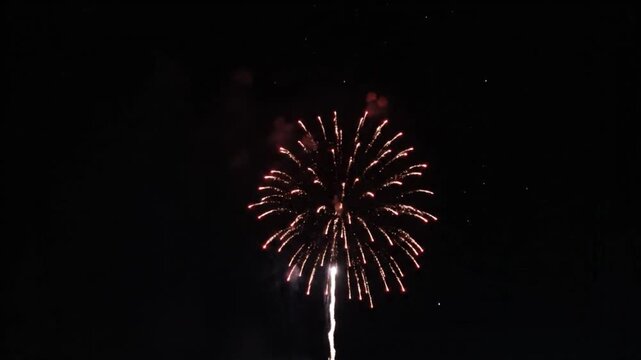 Stunning single firework exploding in the night sky with a vibrant red and white burst of light, creating a dazzling display