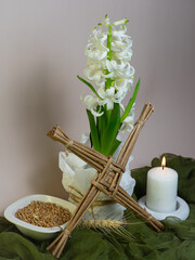 A Saint Brigid’s Day altar with a woven Brigid’s cross, white candles, grains, and a blooming white hyacinth stands on a soft pink‑gray background representing Imbolc purity and new beginnings.