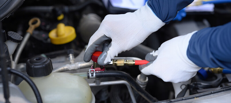 The focus is on the technician's hands inspecting the car's air conditioning system and sizing the equipment for refilling the refrigerant in the car's AC system.