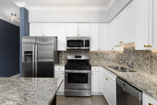 A kitchen with white cabinets, brown and black speckled countertop and backsplash, crown moulding, and grey and blue walls.