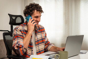 Happy young businessman using smartphone and laptop while enjoying working remotely at his cozy home.	