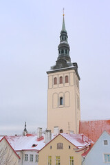 Obraz premium Clock tower of Saint Nicholas church over the snow covered roofs of medieval houses on a cold winter evening in Tallinn, Estonia 