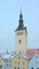 Clock tower of Saint Nicholas church over the snow covered roofs of medieval houses on a cold winter evening in Tallinn, Estonia 