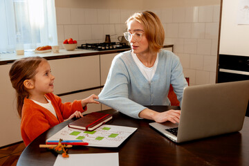 Beautiful woman freelancer working at home, using laptop, sitting at table near little daughter