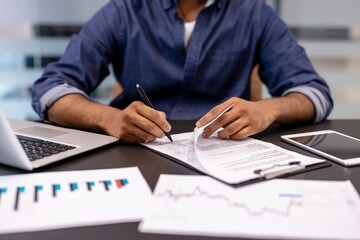 Close-up photo of the hands of a young man sitting at an office desk and signing documents and...