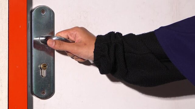 Woman opening house door with hand on metal handle. Close up action showing entry, arrival, and home access concept