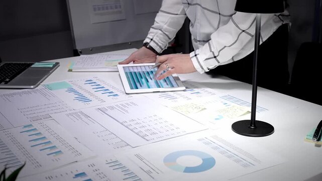 Business professional analyzing corporate financial data using digital tablet and documents, managing workload in late office hours, planning investment strategy and market growth