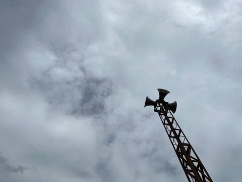 Mosque loudspeaker tower rising into cloudy sky during daytime, emphasizing Islamic call to prayer, community faith, and powerful spiritual symbolism.
