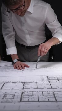Architect working on blueprints using a compass, designing building plans in a studio at night. Concept of architecture and business in low key lighting