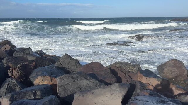 Rocky ocean coastline with breaking waves and blue sky, coastal landscape, ocean waves, rocky shore, blue sky, travel backdrop.
