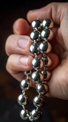 Close Up Of A Hand Holding A Silver Beaded Bracelet With Smooth Spherical Beads And A Soft Focus Background In Warm Lighting