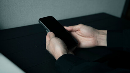 黒いデスクでスマートフォンを操作する両手 スマホ画面を見るビジネスマン モバイルアプリ利用イメージ
