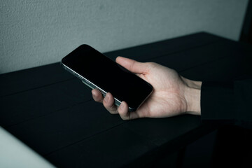 黒いデスクでスマートフォンを操作する両手 スマホ画面を見るビジネスマン モバイルアプリ利用イメージ