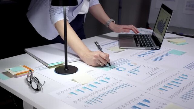Person analyzing financial data, reviewing business analytics reports, using a laptop with charts, and planning corporate strategy with spreadsheets and investment figures