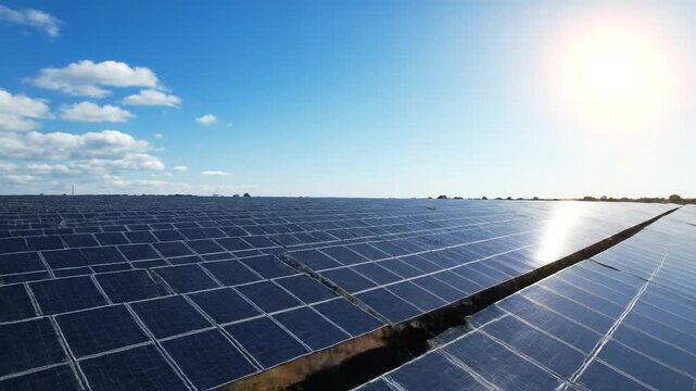 Extensive solar panel array under a bright sun and partly cloudy blue sky, capturing energy