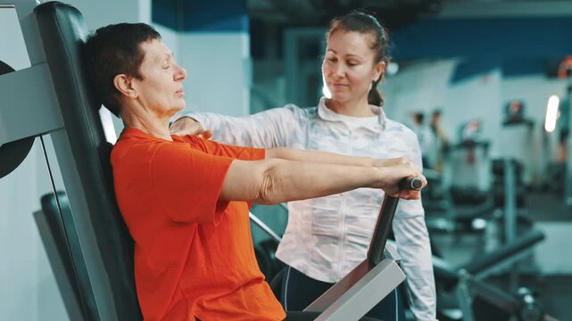 Senior woman exercising on chest press machine with personal trainer