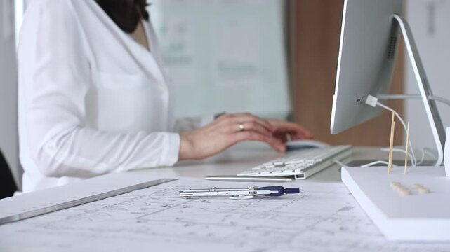 Architect creating new designs, working at a computer in office with blueprints and drafting tools. Business and architecture concept