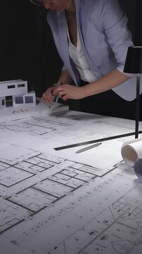 Architect designing building plans on blueprints using a compass, creating residential construction project layout. Architecture and business concept in low key lighting