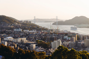 Fototapeta premium Nagasaki panorama, Japan, sunset aerial view, with city skyline, port and mountains, seen from Kazagashira mount park, in spring sunny day with a blue sky, Nagasaki prefecture, Kyushu island region