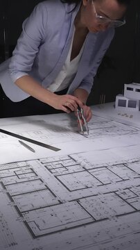 Architect designing building plans on blueprints using a compass, creating residential construction project layout. Architecture and business concept in low key lighting