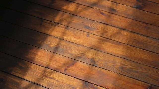 Wooden floor with diagonal sunbeams casting shadows and warm light on polished surface.